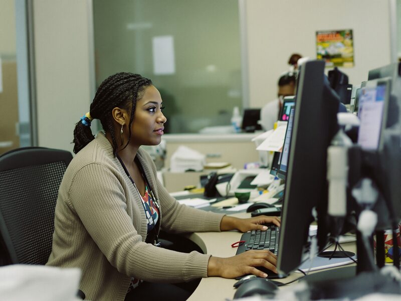 A healthcare administrator working at a computer in a modern hospital office.